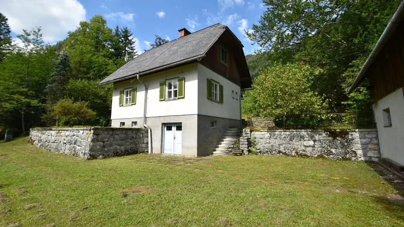 Traditionelles Haus mit weißer Fassade, grünen Fensterläden und Satteldach in ländlicher Umgebung.