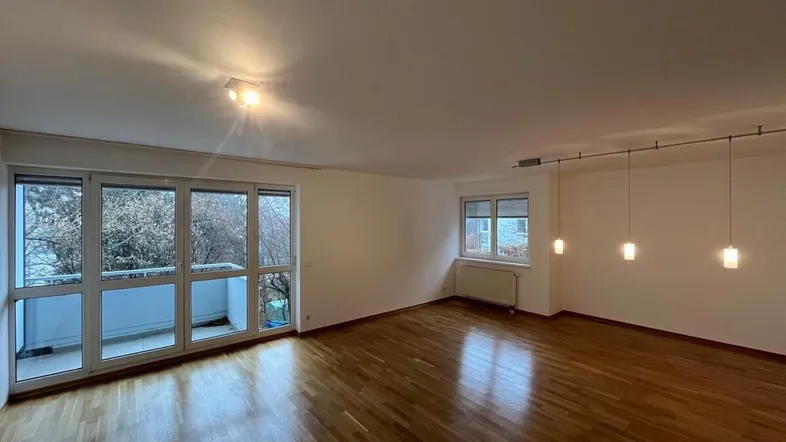 Helles Wohnzimmer mit Parkettboden und Zugang zu einem Balkon mit Blick ins Grüne.