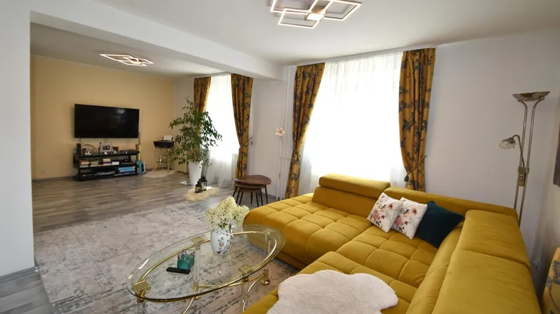 Geräumiges Wohnzimmer mit gelbem Ecksofa, Fernseher und modernem Deckenlicht.