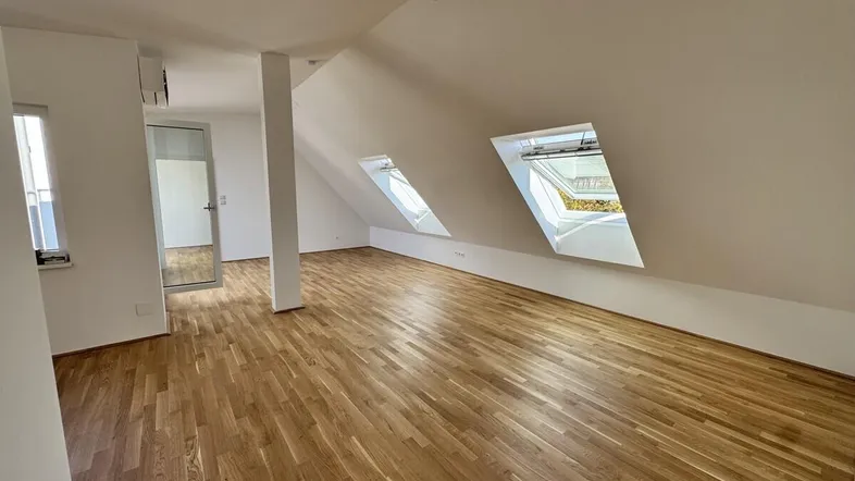 Heller Dachgeschossraum mit Holzboden und Dachfenstern, ideal als Wohn- oder Schlafbereich.