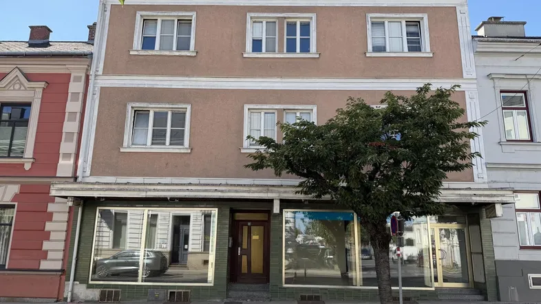 Fassade eines älteren Gebäudes mit Ladenflächen im Erdgeschoss und Wohnungen darüber.