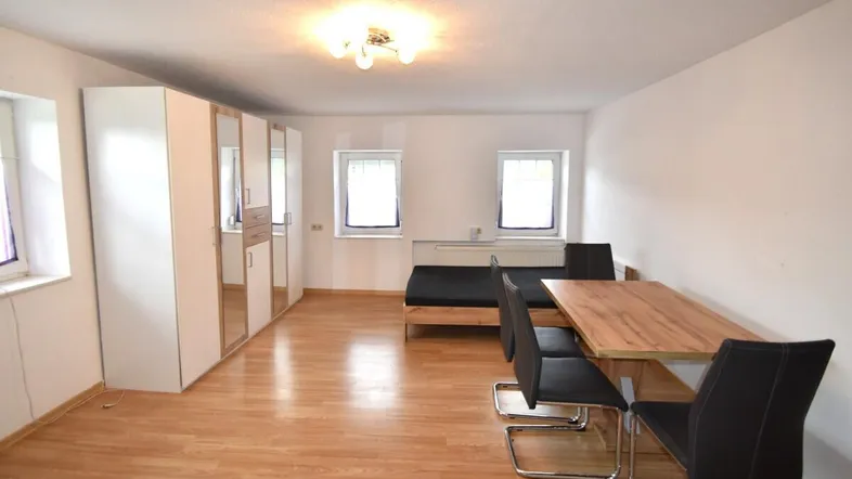 Helles Wohnzimmer mit Holzfußboden, einem Esstisch und einem Bettbereich.
