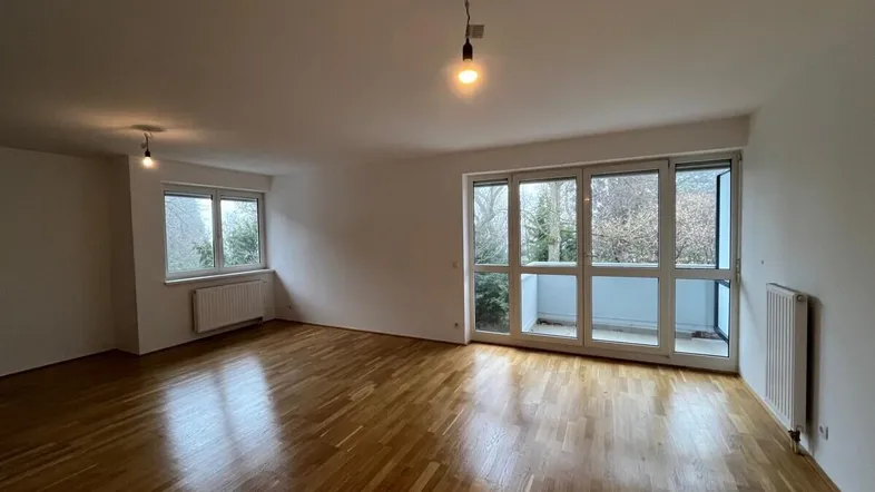 Helles Wohnzimmer mit Parkettboden, weißen Wänden und Zugang zu einem Balkon.