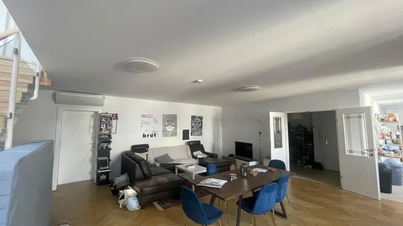 Geräumiger Wohn-Essbereich mit Parkettboden, bequemer Couch, Esstisch und Zugang zu einer Treppe.
