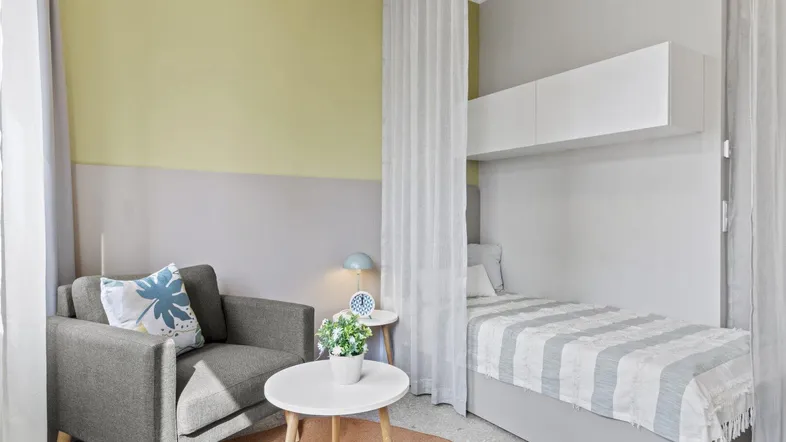 Heller Wohn- und Schlafbereich mit gemütlichem Sessel und modernem Einzelbett in einem Studio.
