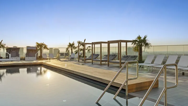 Dachterrasse mit Infinity-Pool, Liegestühlen und Palmen unter klarem Himmel.
