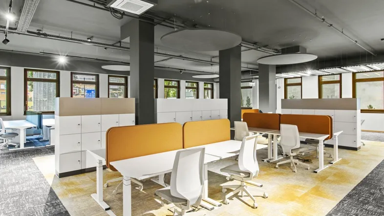 Moderner Großraumbüro mit ergonomischen Arbeitsplätzen, Teppichboden und sichtbaren Deckeninstallationen.