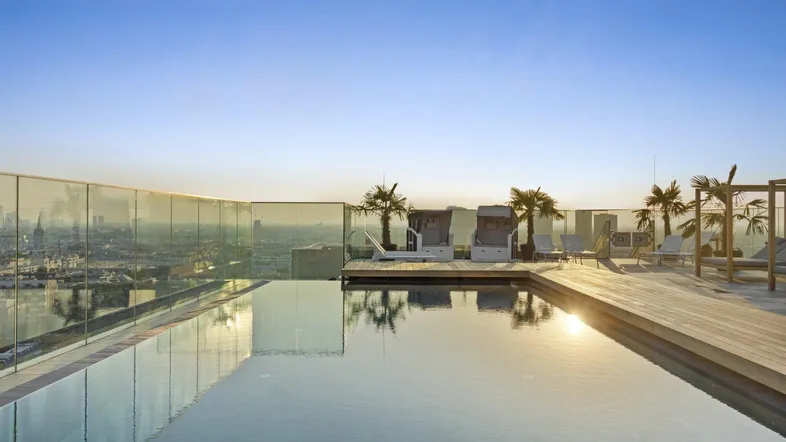 Dachterrasse mit Infinity-Pool, Liegestühlen und Panoramablick über die Stadt bei Sonnenuntergang.
