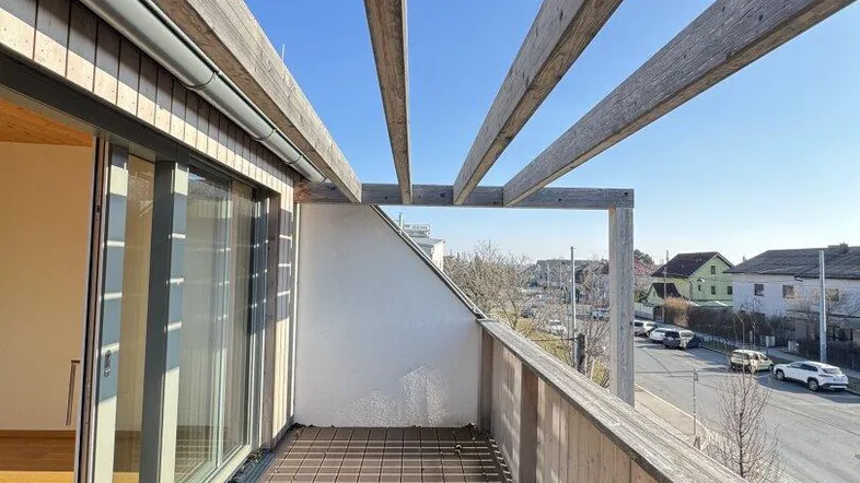 Geräumiger Balkon mit Holzbelag und Pergola, bietet einen Blick auf die Umgebung.