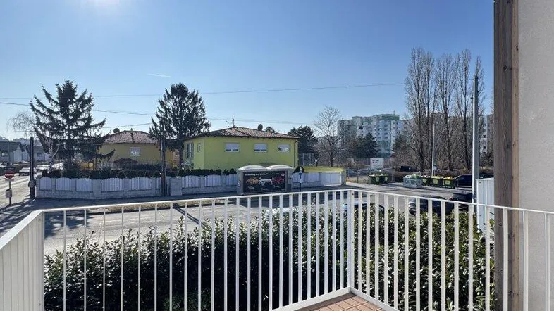 Heller Balkon mit Holzboden und Blick auf die Umgebung an einem sonnigen Tag.