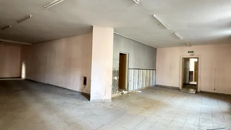 Großer, leerer Raum mit Fliesenboden und sichtbaren Gebrauchsspuren an den Wänden, bereit zur Renovierung.