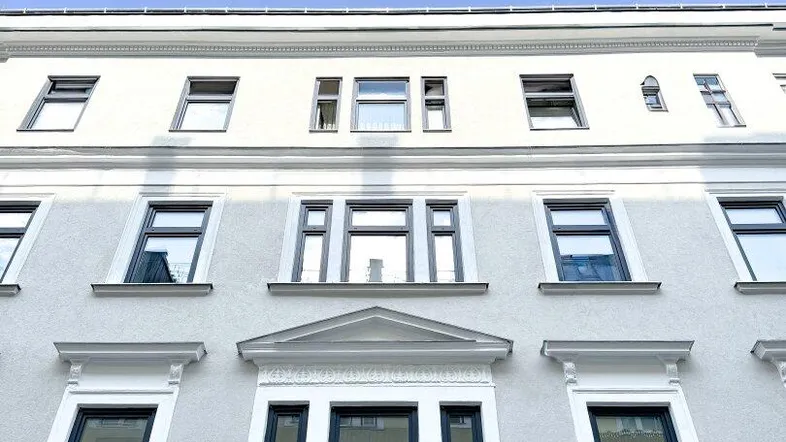 Fassade eines modernen Gebäudes mit großen Fenstern und dekorativen Elementen unter blauem Himmel.