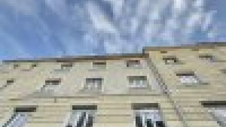 Fassade eines Mehrfamilienhauses mit zahlreichen Fenstern unter einem bewölkten Himmel.