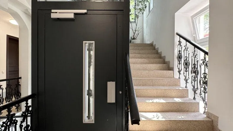 Heller Treppenaufgang mit modernem Aufzug und elegantem schmiedeeisernem Geländer in einem Altbau.