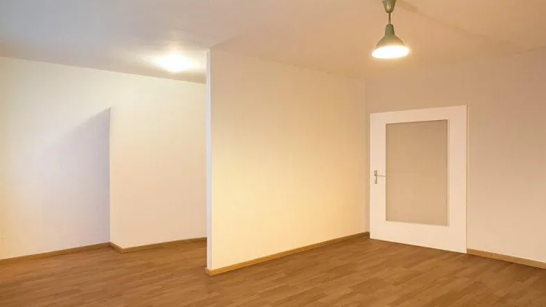 Helles, leeres Zimmer mit Parkettboden und einer Tür mit Milchglas.