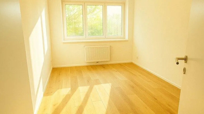 Helles Zimmer mit Holzboden und Fenster, das viel Tageslicht hereinlässt.