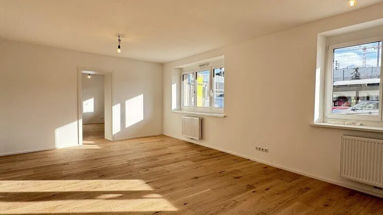 Helles, leeres Zimmer mit neuem Parkettboden und weißen Wänden, durchflutet von natürlichem Sonnenlicht.