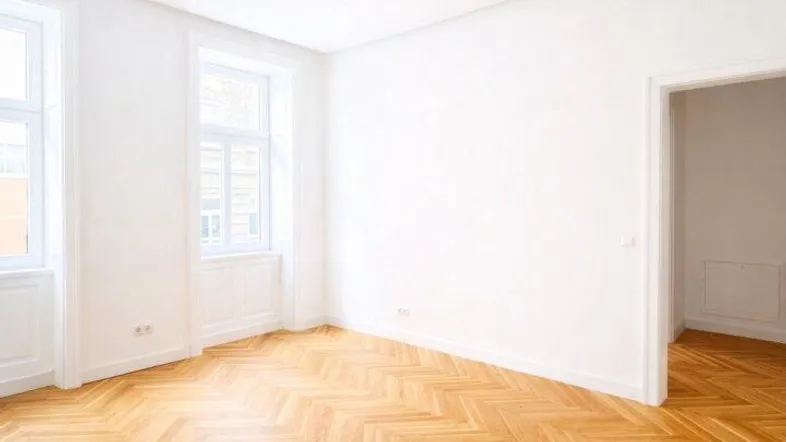 Lichtdurchfluteter Raum mit klassischem Fischgrätparkett und Zugang zu einem weiteren Zimmer.