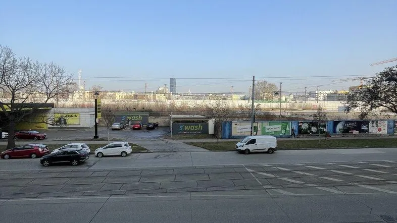 Blick aus dem Fenster auf eine belebte Straße mit parkenden Autos und urbaner Skyline im Hintergrund.