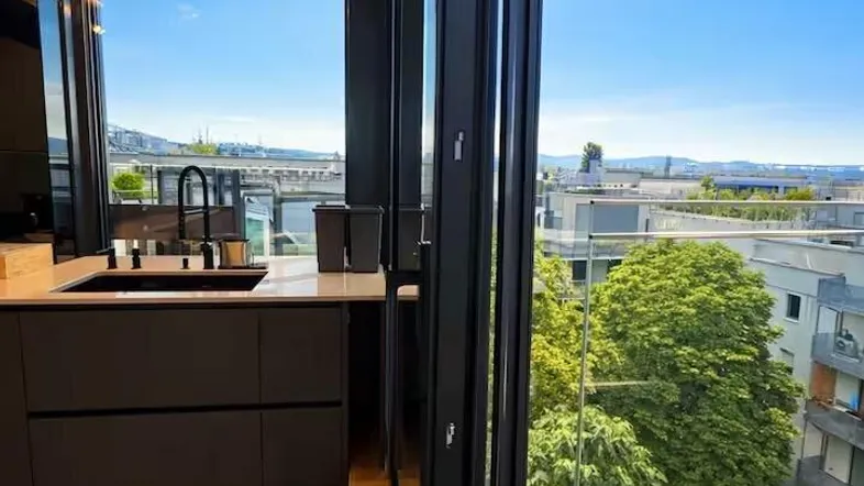 Moderne Küche mit Blick auf die Stadt und viel Grün durch große Fenster.