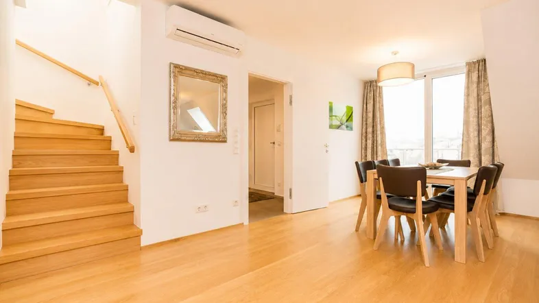 Essbereich mit Holztisch und Stühlen, Treppe und Zugang zu einem weiteren Raum.