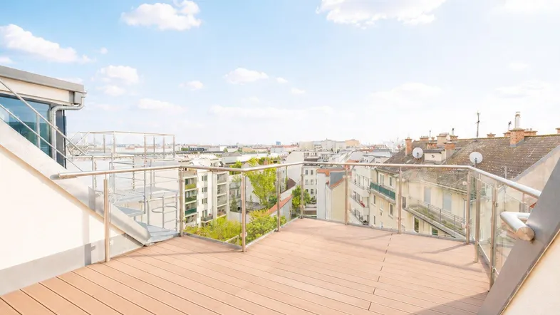 Große Dachterrasse mit Holzboden und Glasgeländer, bietet einen weiten Blick über die Stadt.