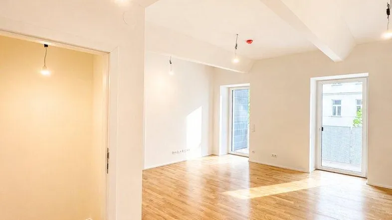 Helles, leeres Zimmer mit Parkettboden und Zugang zu einem Balkon, ideal für Wohnzwecke.