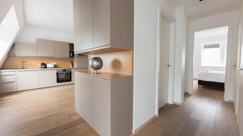 Moderne Küche mit beigefarbenen Schränken, Holzakzenten und Blick in den Flur zum Schlafzimmer.
