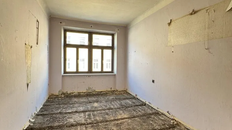 Unrenovierter Innenraum mit sichtbaren Renovierungsspuren, einem Fenster und beschädigten Wänden.