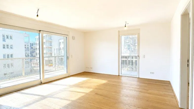 Helles, leeres Wohnzimmer mit großen Schiebetüren und Holzboden, das viel Tageslicht hereinlässt.