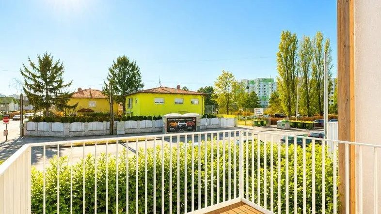Heller Balkon mit Holzboden und weißem Geländer, bietet einen sonnigen Ausblick.