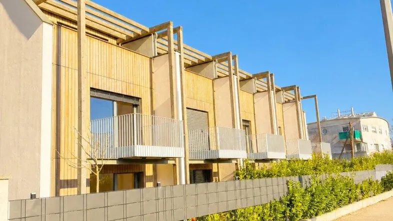 Reihe moderner Stadthäuser mit Holzfassaden, Balkonen und gepflegten Hecken entlang der Straße.