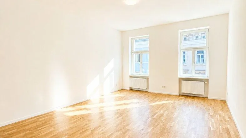Helles, leeres Zimmer mit Eichenparkettboden und zwei Fenstern, das viel Tageslicht hereinlässt.