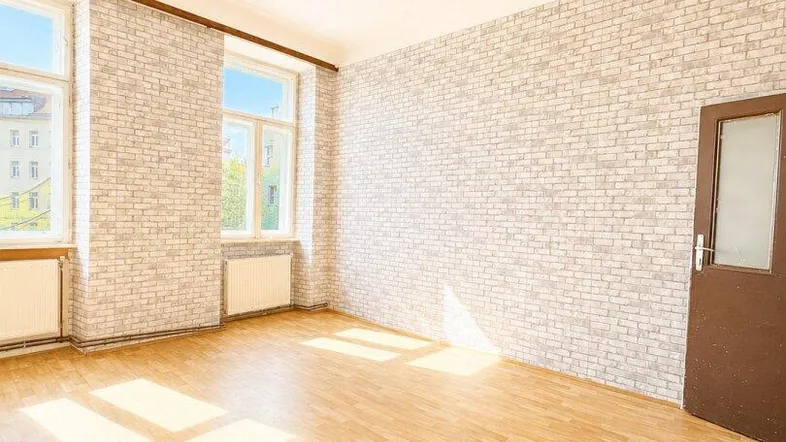 Helles Zimmer mit Parkettboden, Ziegelstein-Tapete und zwei großen Fenstern.