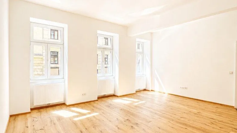 Helles, geräumiges Wohnzimmer mit neu verlegtem Holzboden und hohen Decken, durchflutet von Tageslicht.