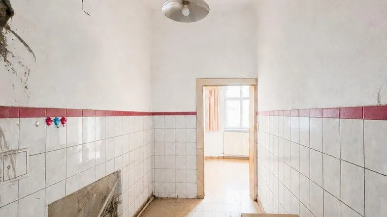 Langer, schmaler Raum mit Fliesen an den Wänden und sichtbaren Wasserschäden an der Decke, renovierungsbedürftig.