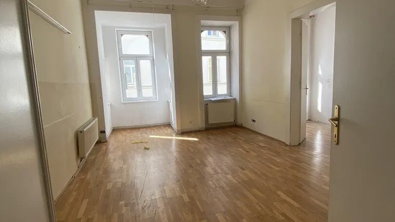 Helles, leeres Wohnzimmer mit Parkettboden, hohen Decken und Kronleuchter, bereit zur individuellen Gestaltung.
