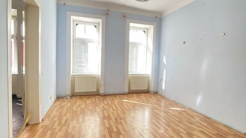 Geräumiges Zimmer in einem Altbau mit Parkettboden und hellblauen Wänden, bereit zur Renovierung.