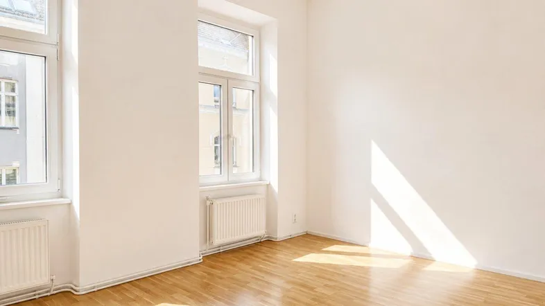 Helles Zimmer mit Parkettboden und großen Fenstern, durch die Sonnenlicht einfällt.