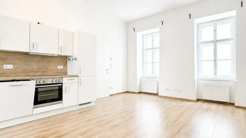 Helles Wohnzimmer mit integrierter Küche, Laminatboden und großen Fenstern.