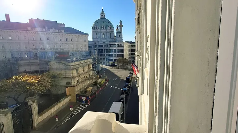 Sonniger Ausblick von einem Balkon auf eine belebte Straße mit historischen Gebäuden und einer Kirche im Hintergrund.