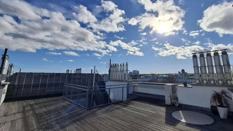 Große Dachterrasse mit Holzboden und weitem Blick über die Stadt unter blauem Himmel.