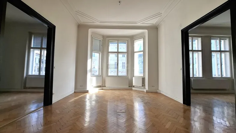 Helles Wohnzimmer mit Fischgrätparkett, hohen Decken und Erkerfenstern, die viel Tageslicht hereinlassen.