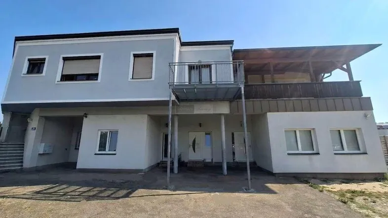 Vorderansicht des Gebäudes mit einem kleinen Balkon und einer überdachten Terrasse im Obergeschoss.