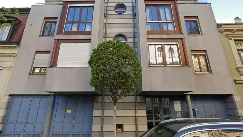 Moderne Fassade eines Mehrfamilienhauses mit großen Fenstern, Garagen und einem Baum davor.