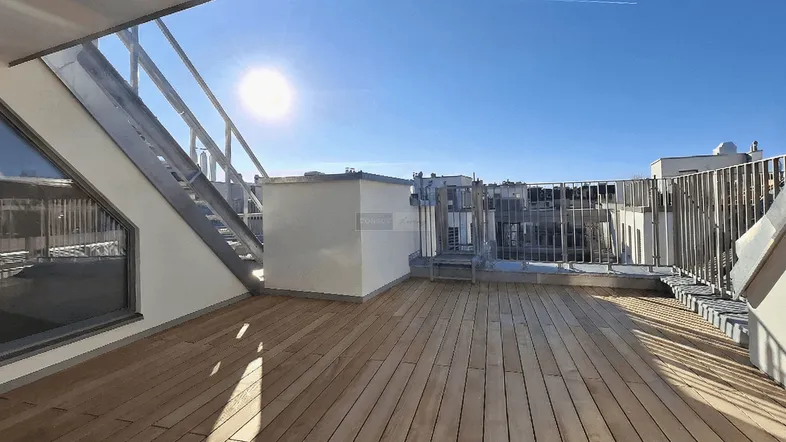 Sonnige Dachterrasse mit Holzboden und weitem Blick über die Stadt und den blauen Himmel.