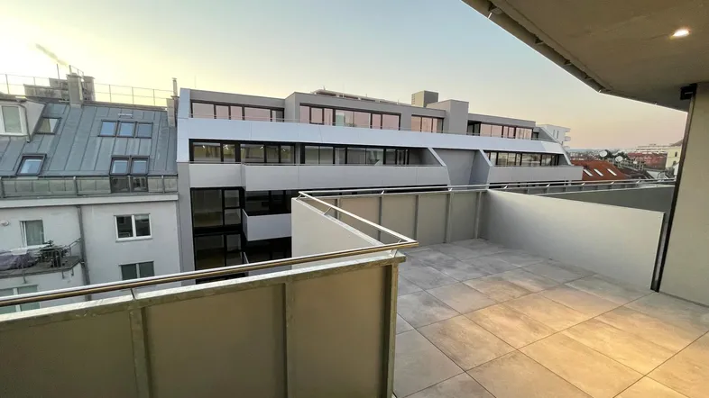 Geräumige Dachterrasse mit Fliesenboden und Blick auf die umliegenden Gebäude bei Sonnenuntergang.