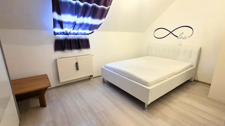 Helles Schlafzimmer im Dachgeschoss mit weißem Bett, schrägen Wänden und Holzboden.