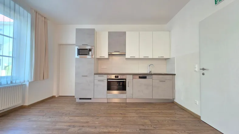 Moderne Einbauküche mit hellen Fronten, integrierten Geräten und Laminatboden in einem offenen Raum.
