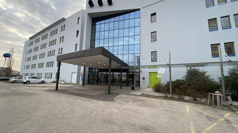 Modernes Bürogebäude mit großer Glasfassade und überdachtem Eingangsbereich unter bewölktem Himmel.